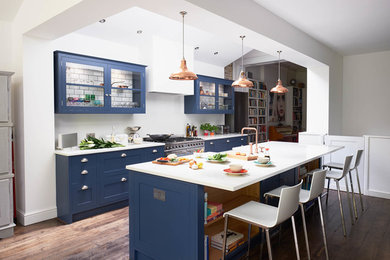 Large contemporary single-wall kitchen/diner in London with a double-bowl sink, shaker cabinets, blue cabinets, quartz worktops, white splashback, stainless steel appliances, an island, stone slab splashback, dark hardwood flooring and brown floors.