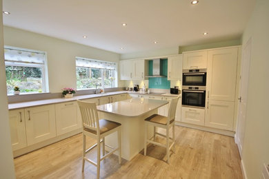 Photo of a large contemporary enclosed kitchen in Essex with shaker cabinets, beige cabinets, quartz worktops, green splashback, glass sheet splashback, stainless steel appliances, an island and a built-in sink.