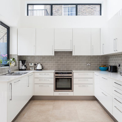 Kitchen - contemporary u-shaped kitchen idea in London with a double-bowl sink, flat-panel cabinets, white cabinets and gray backsplash