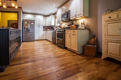 Mittelgroße Klassische Wohnküche in U-Form mit profilierten Schrankfronten, weißen Schränken, Küchengeräten aus Edelstahl, braunem Holzboden und Kücheninsel in St. Louis