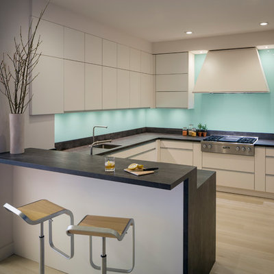 Mid-sized trendy u-shaped light wood floor and beige floor kitchen photo in San Francisco with an undermount sink, flat-panel cabinets, blue backsplash, stainless steel appliances, a peninsula, black countertops, beige cabinets, soapstone countertops and glass sheet backsplash