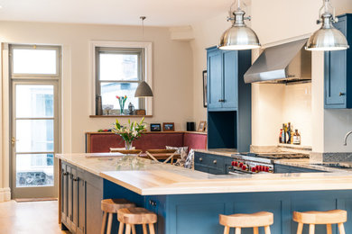 Design ideas for a large traditional u-shaped enclosed kitchen in Other with an integrated sink, shaker cabinets, blue cabinets, granite worktops, white splashback, ceramic splashback, stainless steel appliances, light hardwood flooring, a breakfast bar and multicoloured worktops.
