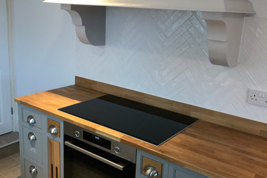 This is an example of a small classic galley kitchen/diner in Other with a belfast sink, shaker cabinets, grey cabinets, wood worktops, white splashback, ceramic splashback, black appliances, vinyl flooring, no island, grey floors and brown worktops.