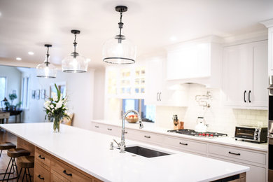 Example of a mid-sized transitional single-wall dark wood floor and brown floor enclosed kitchen design in Boston with an undermount sink, shaker cabinets, white cabinets, quartz countertops, white backsplash, subway tile backsplash, stainless steel appliances and an island
