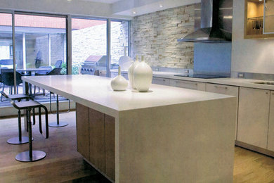 Mittelgroße Moderne Wohnküche in L-Form mit Doppelwaschbecken, flächenbündigen Schrankfronten, beigen Schränken, Küchenrückwand in Weiß, Küchengeräten aus Edelstahl, hellem Holzboden und Kücheninsel in Toronto