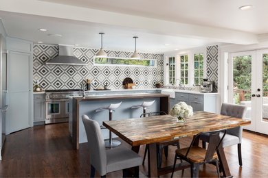 Example of a large trendy l-shaped medium tone wood floor and brown floor eat-in kitchen design in Portland with a farmhouse sink, shaker cabinets, gray cabinets, quartz countertops, gray backsplash, cement tile backsplash, stainless steel appliances, an island and white countertops