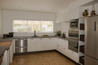Inredning av ett modernt mellanstort kök, med en nedsänkt diskho, släta luckor, vita skåp, laminatbänkskiva, rostfria vitvaror, ljust trägolv och brunt golv