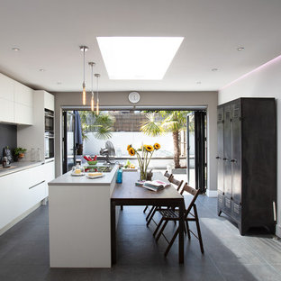 Design ideas for a large contemporary single-wall kitchen in London with an island, a submerged sink, flat-panel cabinets, white cabinets, grey splashback, stainless steel appliances, grey floors, grey worktops and glass sheet splashback.