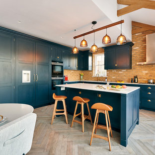 Design ideas for a large eclectic l-shaped open plan kitchen in London with an integrated sink, shaker cabinets, blue cabinets, quartz benchtops, brick splashback, panelled appliances, medium hardwood floors, with island and white benchtop.