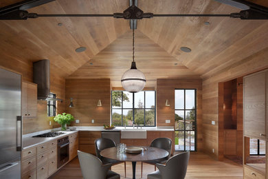 Large mountain style l-shaped medium tone wood floor and beige floor eat-in kitchen photo in San Francisco with flat-panel cabinets, medium tone wood cabinets, stainless steel appliances, a farmhouse sink, brown backsplash, wood backsplash and no island