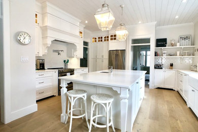 Enclosed kitchen - large cottage u-shaped medium tone wood floor and brown floor enclosed kitchen idea in Other with an undermount sink, shaker cabinets, white cabinets, quartz countertops, white backsplash, subway tile backsplash, stainless steel appliances, an island and white countertops