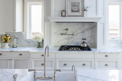 Inredning av ett klassiskt vit vitt kök och matrum, med en rustik diskho, vita skåp, marmorbänkskiva, vitt stänkskydd, stänkskydd i marmor, rostfria vitvaror, mörkt trägolv, en köksö och brunt golv