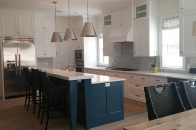 Inspiration for a mid-sized coastal l-shaped dark wood floor and brown floor eat-in kitchen remodel in Minneapolis with shaker cabinets, white cabinets, solid surface countertops, gray backsplash, stone tile backsplash, stainless steel appliances and an island