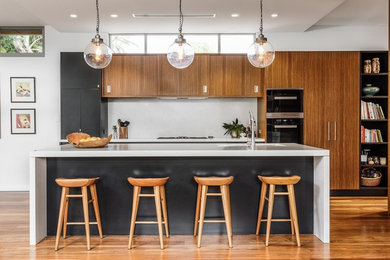 Idée de décoration pour une cuisine ouverte parallèle design de taille moyenne avec un évier encastré, une crédence grise, un électroménager noir, un sol en bois brun et îlot.