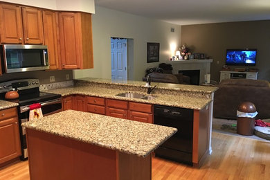 Mid-sized trendy l-shaped yellow floor open concept kitchen photo in Philadelphia with a double-bowl sink, raised-panel cabinets, light wood cabinets, granite countertops, black appliances and an island
