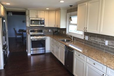 Mid-sized transitional single-wall dark wood floor enclosed kitchen photo in Providence with a double-bowl sink, recessed-panel cabinets, white cabinets, granite countertops, gray backsplash, matchstick tile backsplash, stainless steel appliances and a peninsula