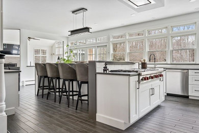 Transitional porcelain tile kitchen photo in Providence with a farmhouse sink, shaker cabinets, white cabinets, quartz countertops, white backsplash, subway tile backsplash, stainless steel appliances and an island