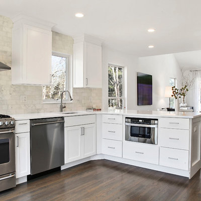 Open concept kitchen - transitional l-shaped dark wood floor and brown floor open concept kitchen idea in New York with an undermount sink, flat-panel cabinets, white cabinets, white backsplash, subway tile backsplash, stainless steel appliances, a peninsula, solid surface countertops and white countertops