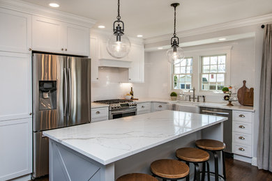 Eat-in kitchen - mid-sized cottage l-shaped dark wood floor and brown floor eat-in kitchen idea in New York with a farmhouse sink, shaker cabinets, white cabinets, quartz countertops, white backsplash, subway tile backsplash, stainless steel appliances, an island and white countertops