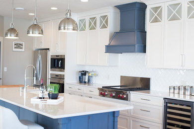 Example of a large beach style galley light wood floor open concept kitchen design in Other with a farmhouse sink, recessed-panel cabinets, white cabinets, white backsplash, subway tile backsplash, stainless steel appliances and an island