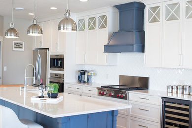 Large nautical galley open plan kitchen in Other with a belfast sink, recessed-panel cabinets, white cabinets, white splashback, metro tiled splashback, stainless steel appliances, light hardwood flooring and an island.