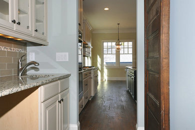 Modelo de cocina comedor lineal de estilo americano con armarios tipo vitrina, puertas de armario beige, encimera de granito, salpicadero gris y salpicadero de azulejos de vidrio