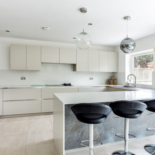 Inspiration for a contemporary u-shaped kitchen in London with a built-in sink, flat-panel cabinets, beige cabinets, white splashback, stainless steel appliances, a breakfast bar, beige floors and white worktops.