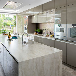 Photo of a mid-sized contemporary galley kitchen in Other with flat-panel cabinets, grey cabinets, solid surface benchtops, glass sheet splashback, stainless steel appliances, porcelain floors, with island, multi-coloured floor, beige benchtop, an integrated sink and beige splashback.