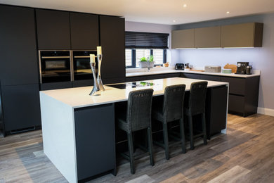 This is an example of a contemporary open plan kitchen in Sussex with flat-panel cabinets, black appliances, an island, multi-coloured floors and white worktops.