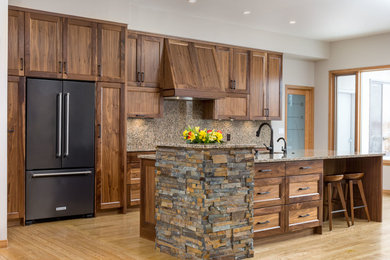 Example of a large mountain style galley light wood floor and multicolored floor open concept kitchen design in Other with an undermount sink, recessed-panel cabinets, medium tone wood cabinets, granite countertops, brown backsplash, stone slab backsplash, black appliances and an island
