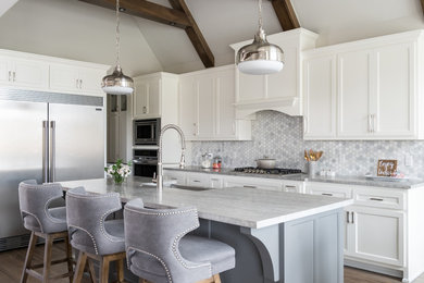 Classic grey and white l-shaped kitchen in Other with a belfast sink, shaker cabinets, white cabinets, white splashback, marble splashback, stainless steel appliances, medium hardwood flooring, an island and brown floors.