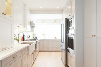 Example of a cottage light wood floor kitchen design in Vancouver with a farmhouse sink, shaker cabinets, quartz countertops, white backsplash, mosaic tile backsplash and stainless steel appliances