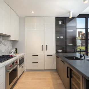 Imagen de cocina contemporánea, de tamaño medio, con puertas de armario blancas, encimera de mármol, fregadero de doble seno, armarios con paneles lisos, salpicadero blanco, salpicadero de mármol, electrodomésticos de acero inoxidable, suelo de madera clara y península