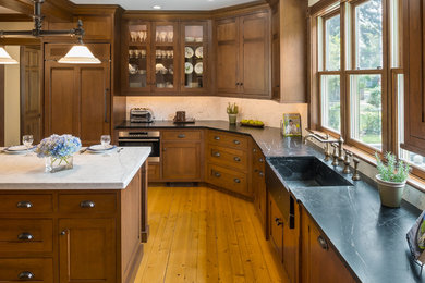Inspiration for a mid-sized timeless u-shaped light wood floor enclosed kitchen remodel in Boston with a farmhouse sink, beaded inset cabinets, dark wood cabinets, soapstone countertops, white backsplash, subway tile backsplash, paneled appliances and an island