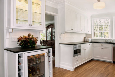 Example of a small transitional galley medium tone wood floor enclosed kitchen design in Portland with an undermount sink, glass-front cabinets, white cabinets, granite countertops, white backsplash, ceramic backsplash, stainless steel appliances and no island