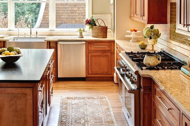 Inredning av ett klassiskt stort kök, med en rustik diskho, skåp i shakerstil, skåp i mellenmörkt trä, granitbänkskiva, beige stänkskydd, stänkskydd i stenkakel, rostfria vitvaror, mellanmörkt trägolv, en köksö och brunt golv