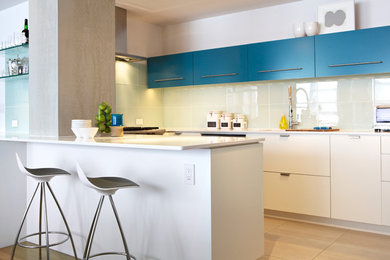 Example of a mid-sized trendy galley porcelain tile eat-in kitchen design in New York with a double-bowl sink, flat-panel cabinets, blue cabinets, quartz countertops, white backsplash, glass tile backsplash, stainless steel appliances and a peninsula