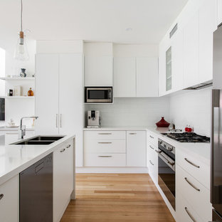 Inspiration for a contemporary u-shaped kitchen in Adelaide with a double-bowl sink, flat-panel cabinets, white cabinets, white splashback, subway tile splashback, stainless steel appliances, medium hardwood floors, a peninsula, brown floor and white benchtop.