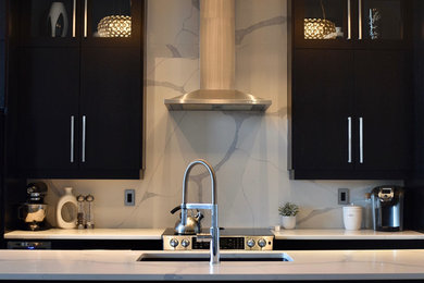Example of a mid-sized trendy single-wall brown floor eat-in kitchen design in Other with granite countertops, an undermount sink, flat-panel cabinets, black cabinets, white backsplash, stone slab backsplash, stainless steel appliances and an island