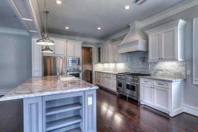 Open concept kitchen - large traditional medium tone wood floor open concept kitchen idea in Houston with a farmhouse sink, shaker cabinets, white cabinets, quartzite countertops, gray backsplash, stone slab backsplash, stainless steel appliances and an island