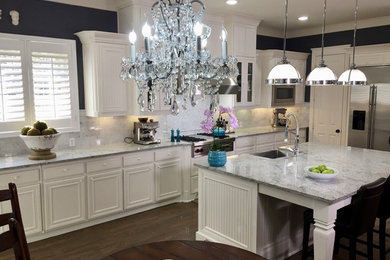 Example of a large transitional u-shaped dark wood floor eat-in kitchen design in Dallas with a farmhouse sink, raised-panel cabinets, white cabinets, granite countertops, white backsplash, stone tile backsplash, stainless steel appliances and an island