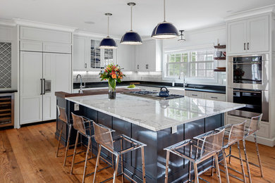 Inspiration for a large transitional l-shaped medium tone wood floor eat-in kitchen remodel in Boston with a farmhouse sink, white backsplash, paneled appliances, an island and shaker cabinets