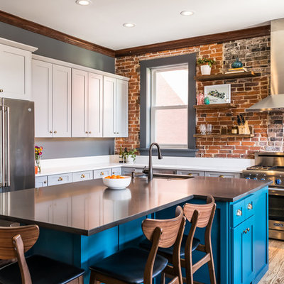 Mid-sized eclectic l-shaped medium tone wood floor and brown floor kitchen photo in St Louis with a single-bowl sink, shaker cabinets, quartz countertops, brick backsplash, stainless steel appliances, an island, white countertops and blue cabinets