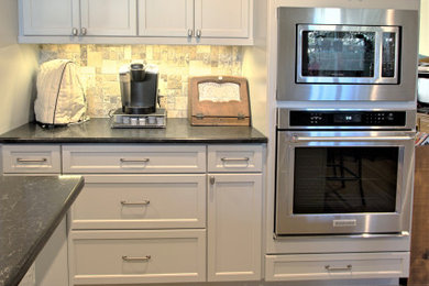 ダラスにあるエクレクティックスタイルのおしゃれなキッチン (白いキャビネット、マルチカラーのキッチンパネル、ライムストーンのキッチンパネル、シルバーの調理設備、茶色い床、黒いキッチンカウンター) の写真