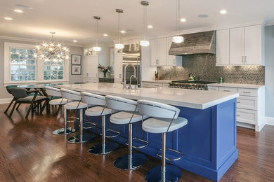 Example of a mid-sized eclectic galley medium tone wood floor and brown floor eat-in kitchen design in New York with a farmhouse sink, shaker cabinets, white cabinets, solid surface countertops, gray backsplash, mosaic tile backsplash, stainless steel appliances, an island and white countertops