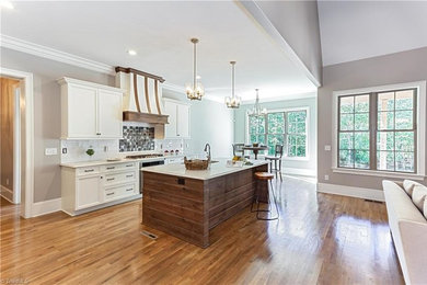 Example of a mid-sized arts and crafts single-wall medium tone wood floor eat-in kitchen design in Raleigh with an undermount sink, flat-panel cabinets, white cabinets, quartz countertops, white backsplash, porcelain backsplash, stainless steel appliances, an island and white countertops