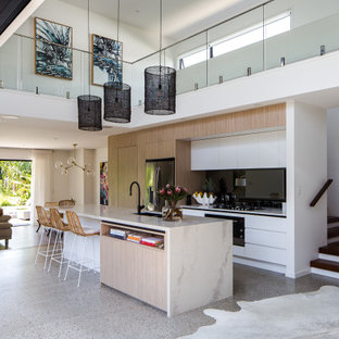 Design ideas for a contemporary galley open plan kitchen in Gold Coast - Tweed with an undermount sink, flat-panel cabinets, white cabinets, black splashback, stainless steel appliances, concrete floors, with island, grey floor and white benchtop.