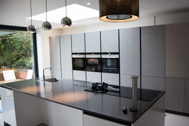 Photo of a large contemporary single-wall kitchen/diner in West Midlands with a single-bowl sink, flat-panel cabinets, grey cabinets, quartz worktops, black appliances, porcelain flooring, an island and grey floors.
