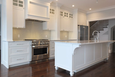Photo of a medium sized traditional galley kitchen in Montreal with a double-bowl sink, white cabinets, marble worktops, white splashback, mosaic tiled splashback, stainless steel appliances, dark hardwood flooring, an island and brown floors.