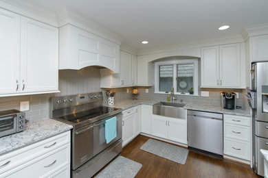 Example of a large transitional l-shaped dark wood floor and brown floor kitchen design in Baltimore with a farmhouse sink, recessed-panel cabinets, white cabinets, quartz countertops, gray backsplash, subway tile backsplash, stainless steel appliances and an island
